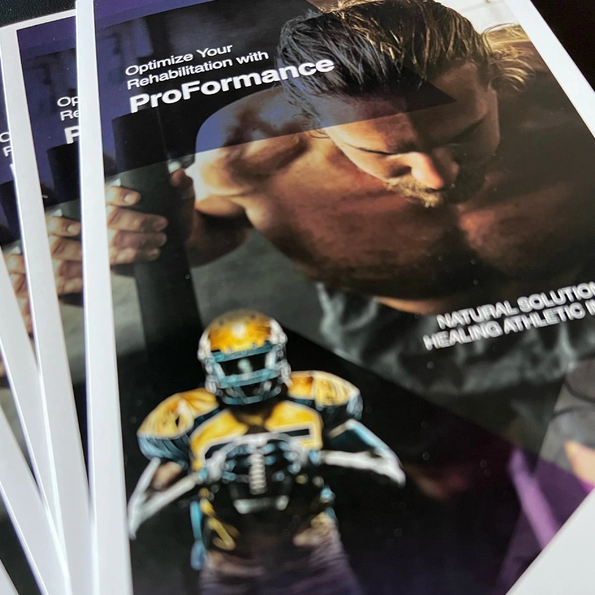 Stack of printed ProFormance brochures: “Optimize Your Rehabilitation with ProFormance” over an athlete training and a football player