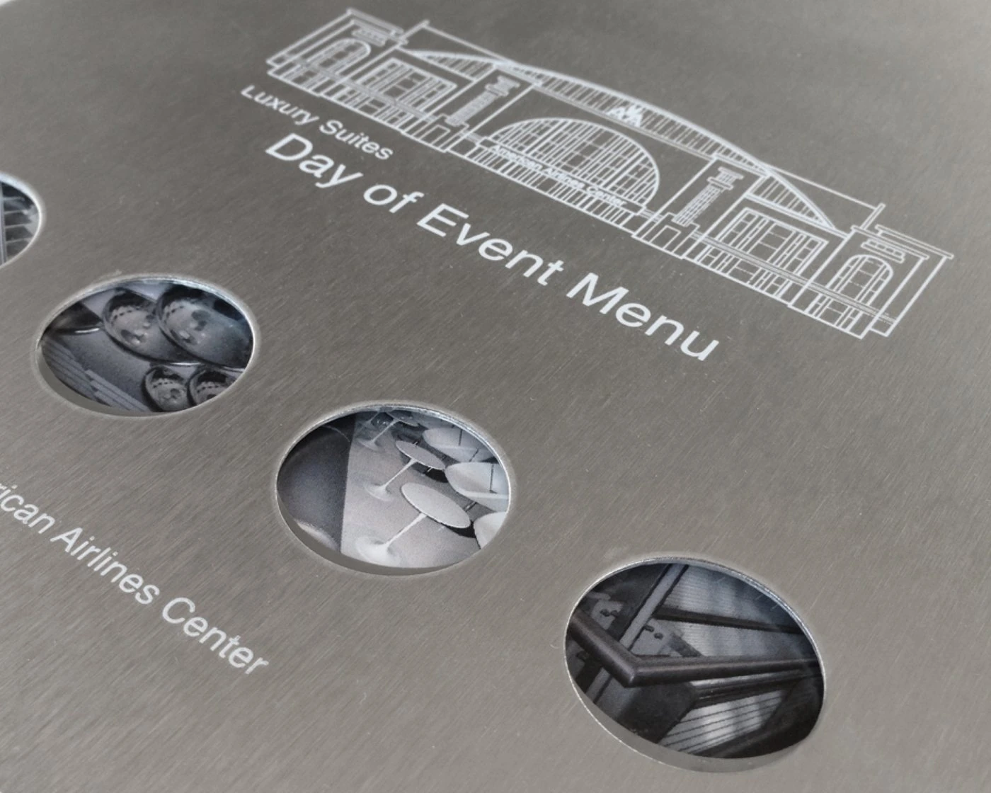 Brushed-metal Day of Event Menu cover with a white line drawing of the arena and die-cut photo circles