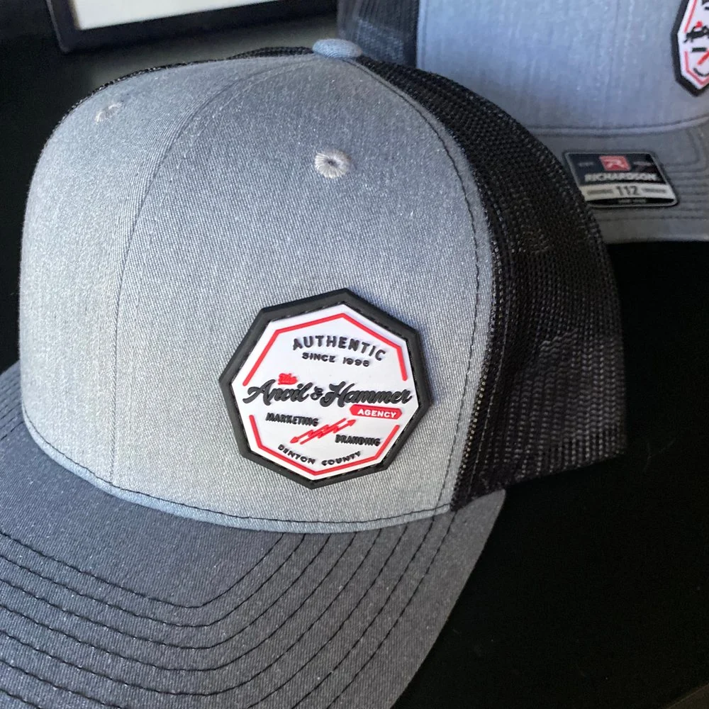 Gray trucker hat with the Anvil & Hammer Agency badge patch