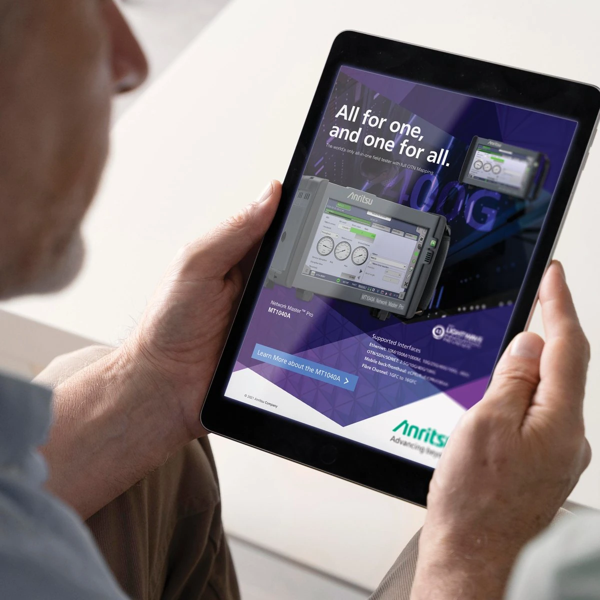 A man holding a tablet showing the Anritsu MT1040A ad “All for one, and one for all.”