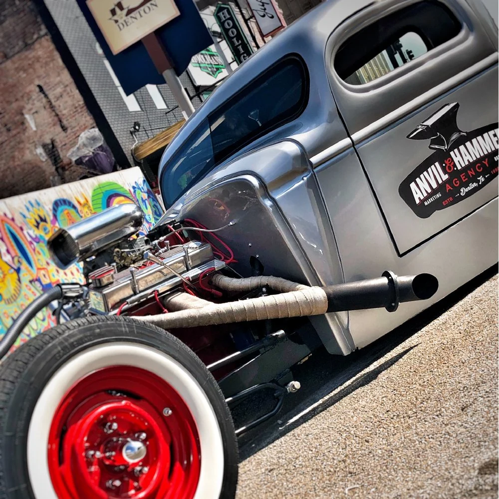 The Anvil & Hammer hot rod, with red wheels and the agency logo on the door, parked on the square in Denton