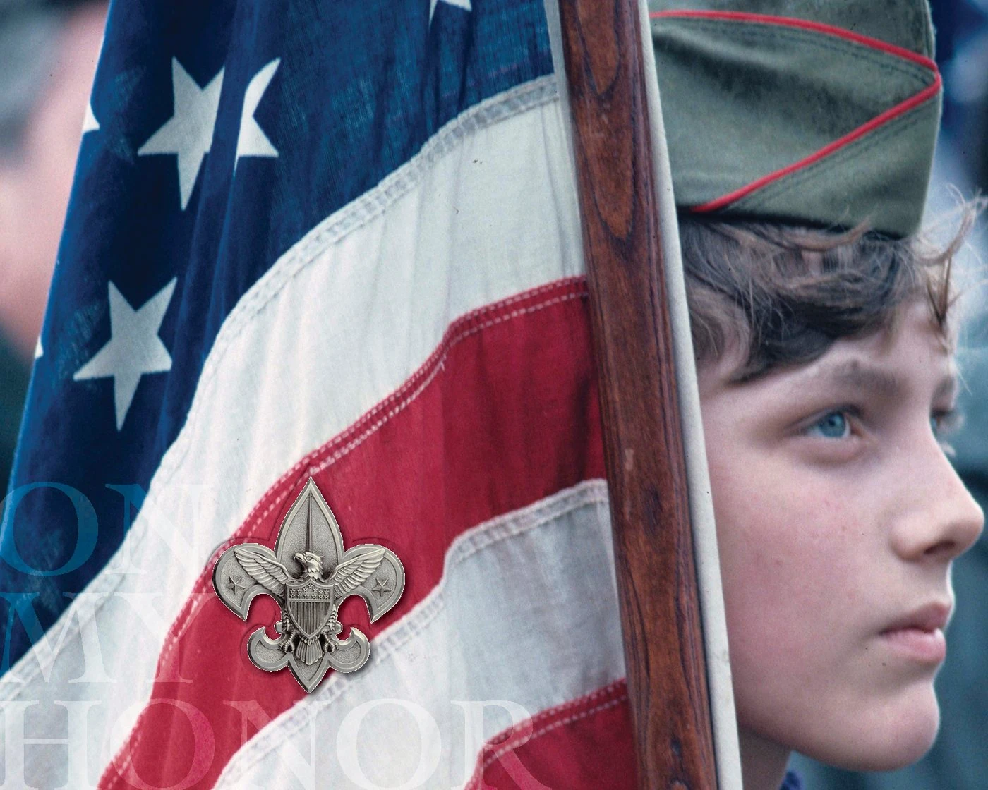 A young Scout holding an American flag, with a silver fleur-de-lis and the words “On my honor”