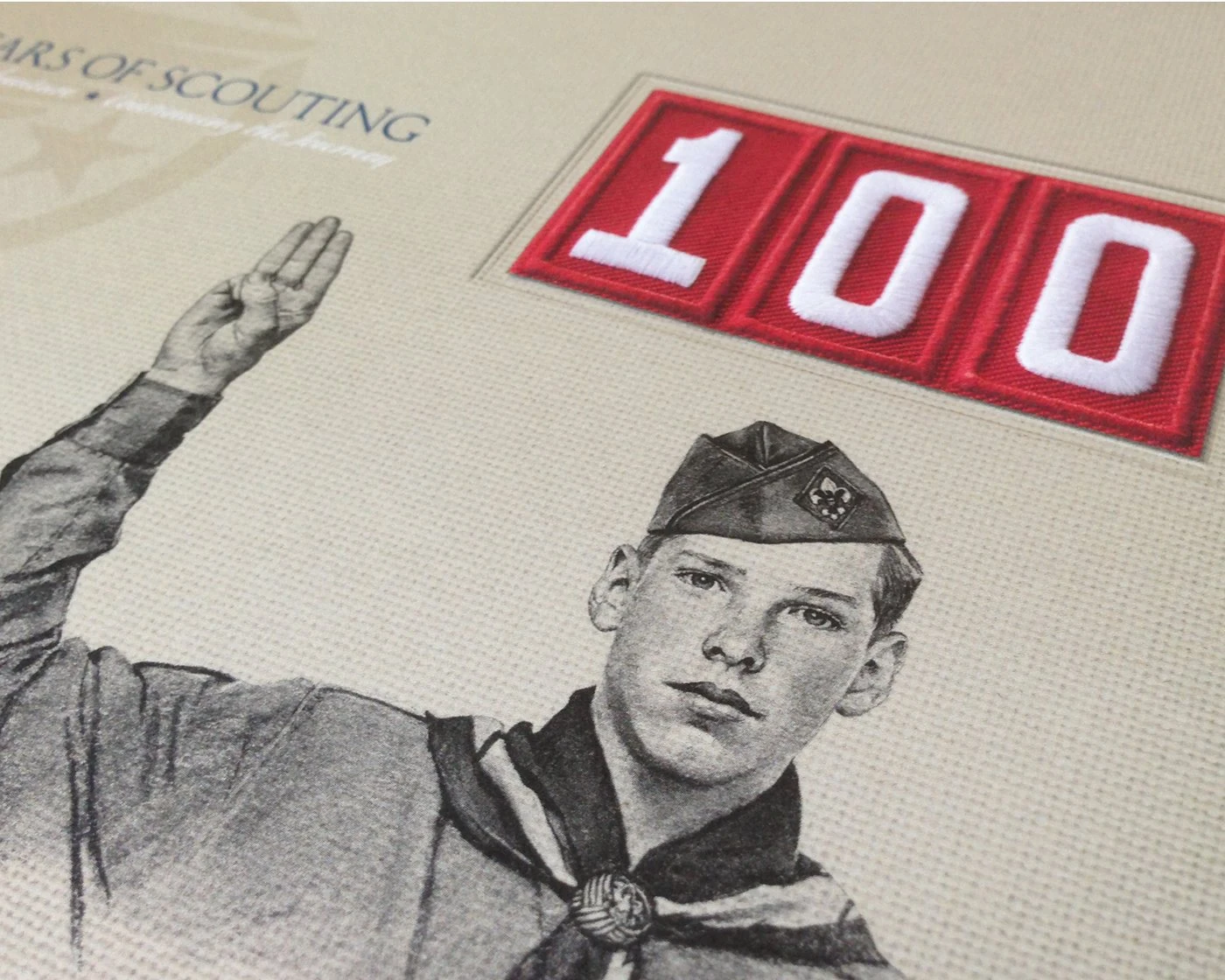 Close-up of the 100 Years of Scouting book cover: an engraved Scout giving the Scout sign beside an embroidered red 100 patch